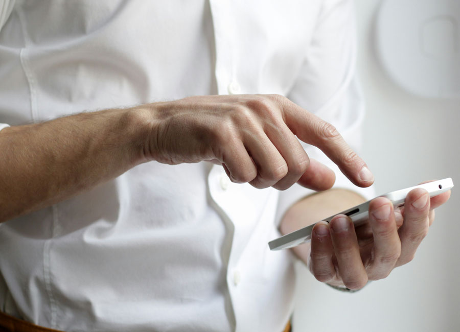 Mann in weißem Hemd tippt auf Smartphone